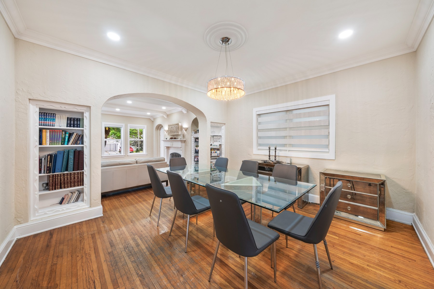 Unit 1, present day. The dining room looking through the original 1925 archway into the living room. Chandelier, plaster bookcase niches built into the walls, Dade County pine floors throughout — the kind of architectural integrity that is very hard to replicate.